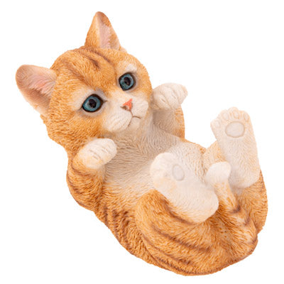 An orange tabby kitten figurine lying on its back with paws raised, featuring large blue eyes and cream-colored paws and chest, isolated on a white background.