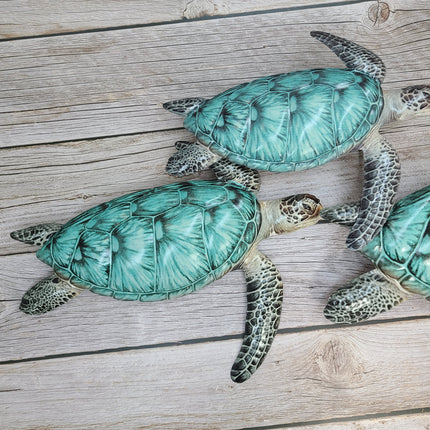 Three aqua blue metal sea turtles swimming in a family group, detailed coastal wall sculpture for beach-themed home decor.