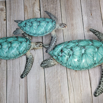 Three aqua blue metal sea turtles swimming in a family group, detailed coastal wall sculpture for beach-themed home decor.